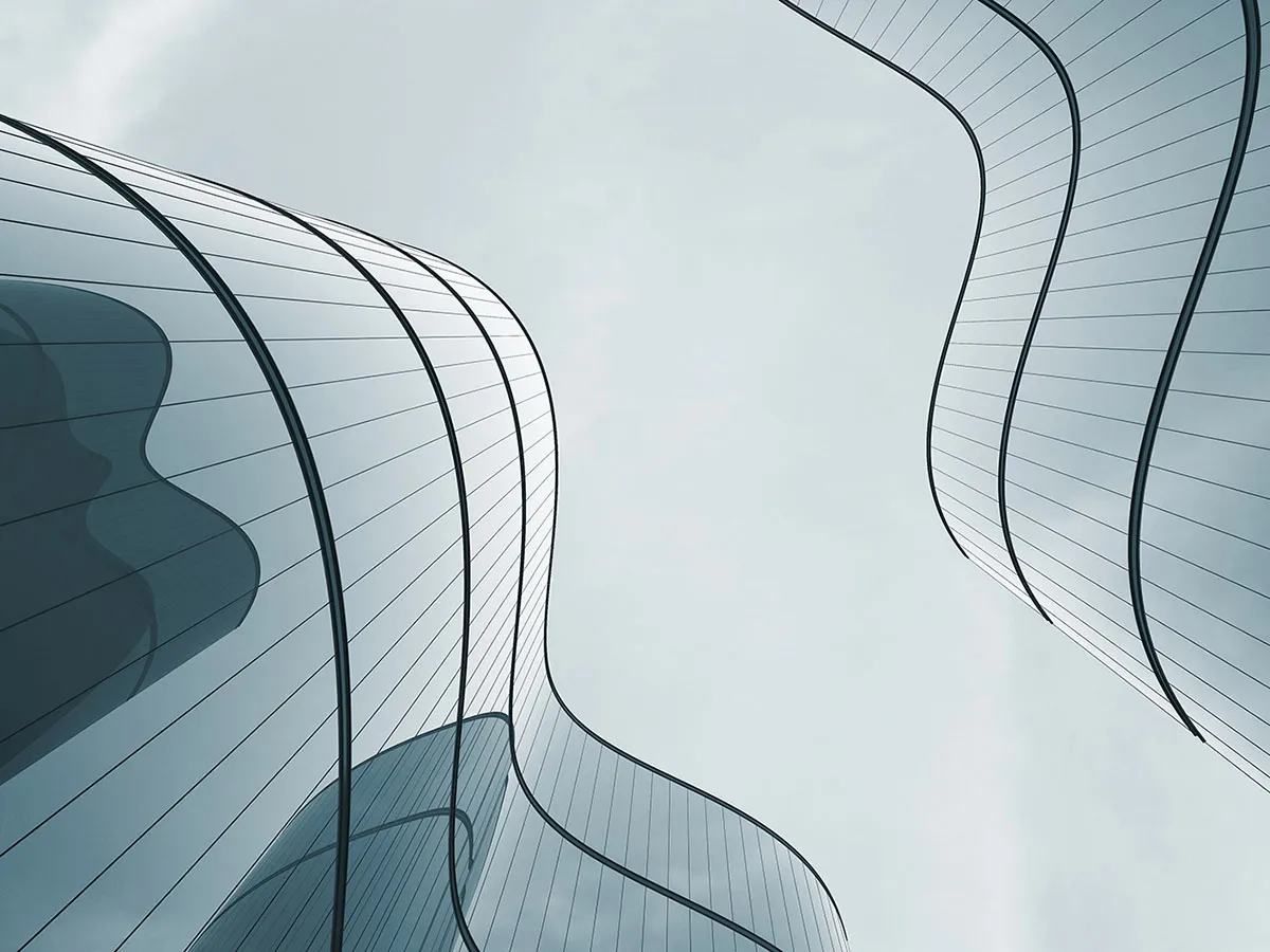 Curved glass skyscrapers with sleek, reflective surfaces rise against a cloudy sky, creating an abstract and futuristic architectural scene.
